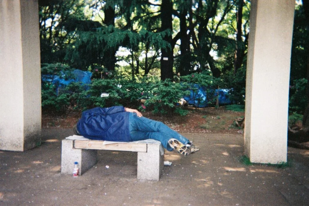 A man lies on an uncomfortably short bench 